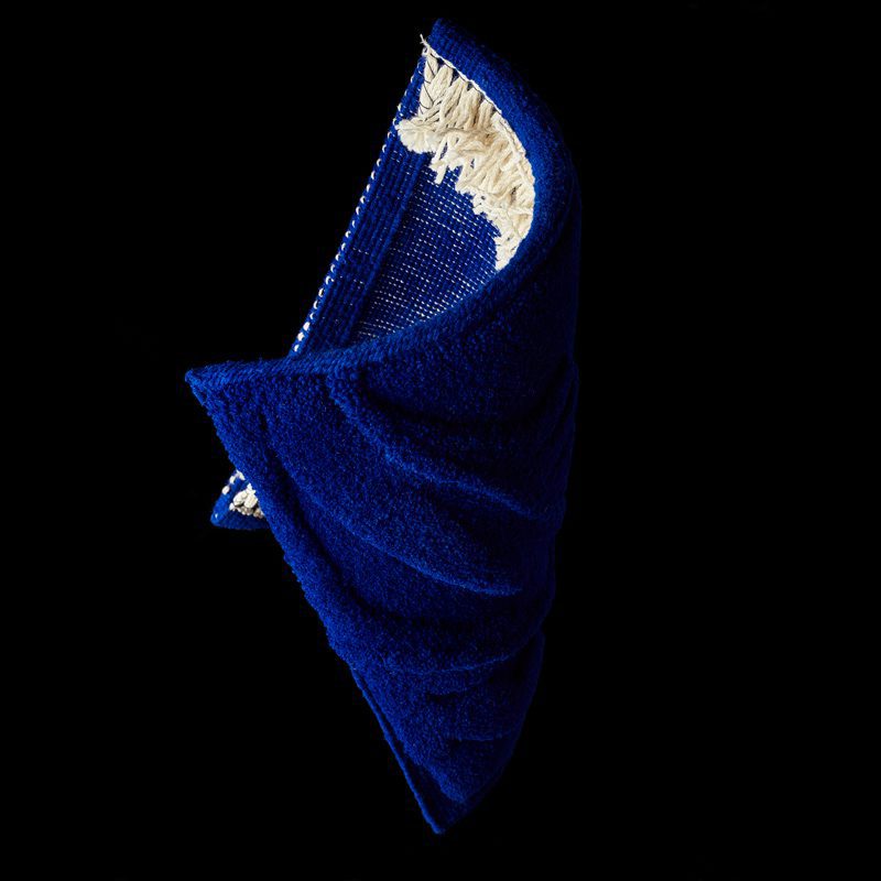 Technique de la Savonnerie pour un velours bleu profond, le carré Métamorphose II lévite sur fond noir.